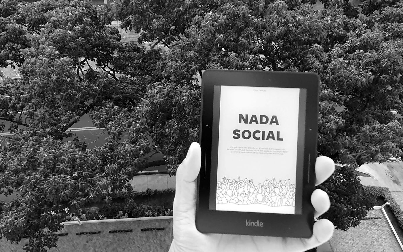 Lector electrónico con la portada del libro Nada Social, sostenido frente a árboles